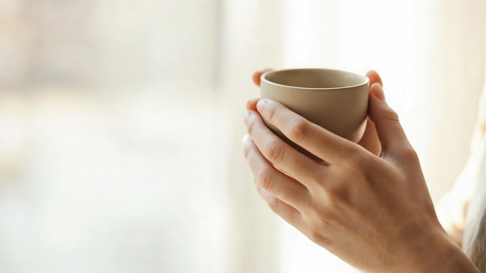Due mani che stringono una tazza di ceramica calda, luce diffusa, nessun volto