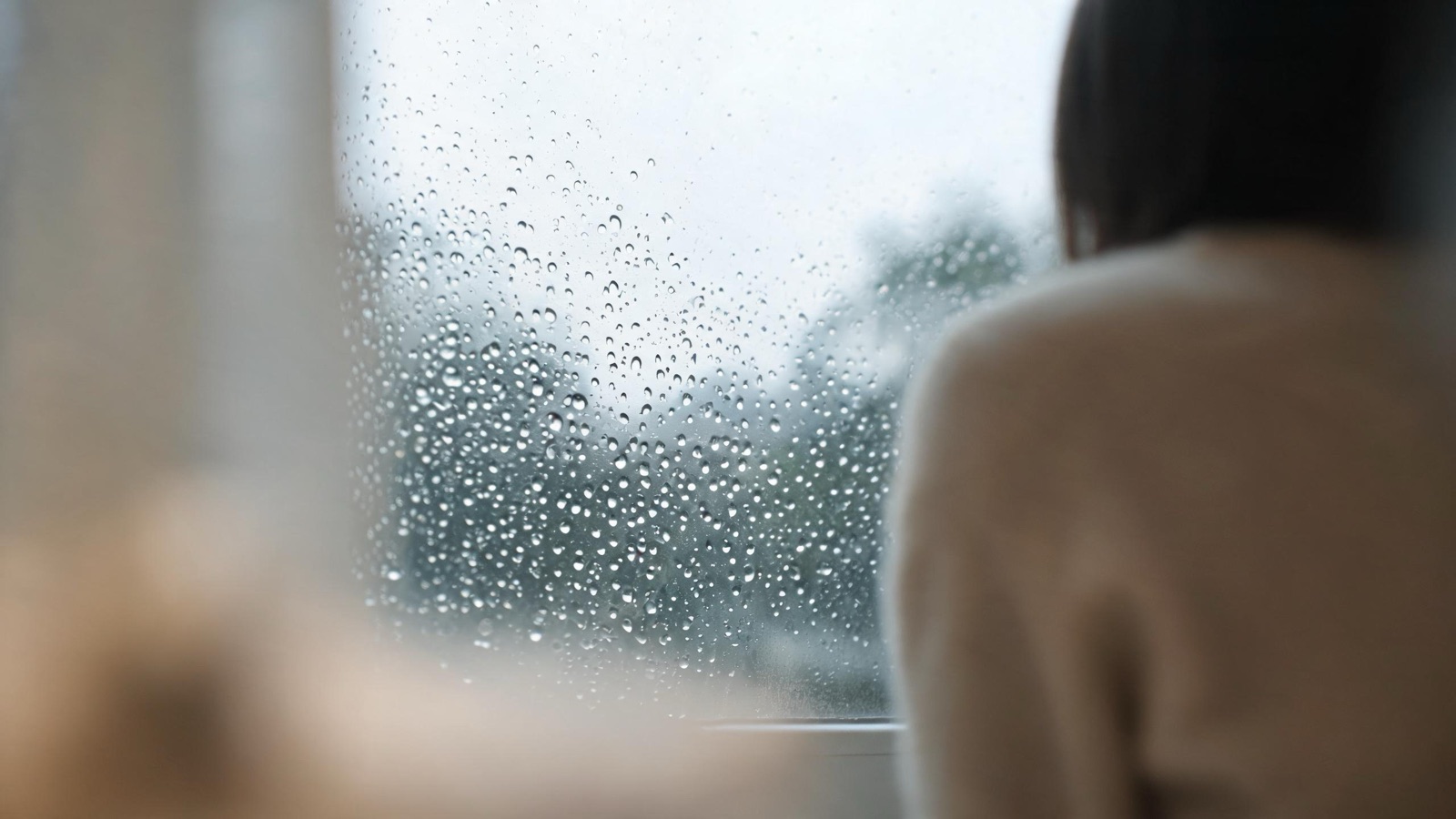 Gocce di pioggia sul vetro di una finestra, luce grigia e tepore sfocato all'interno