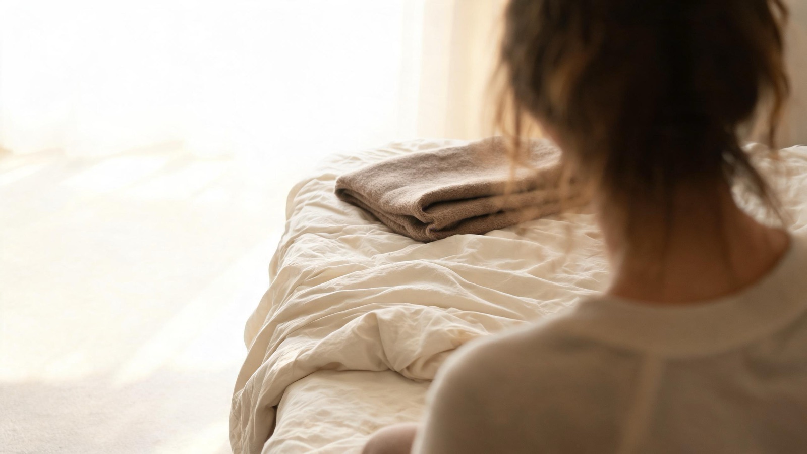 Lenzuola di lino sfatte e una coperta di lana piegata nella luce del primo mattino