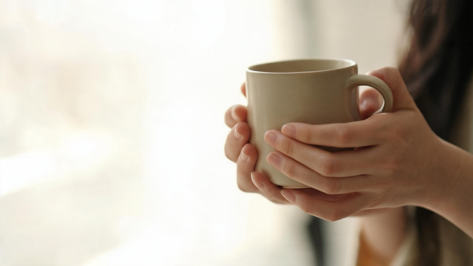 Due mani che stringono una tazza di ceramica calda, luce diffusa, nessun volto