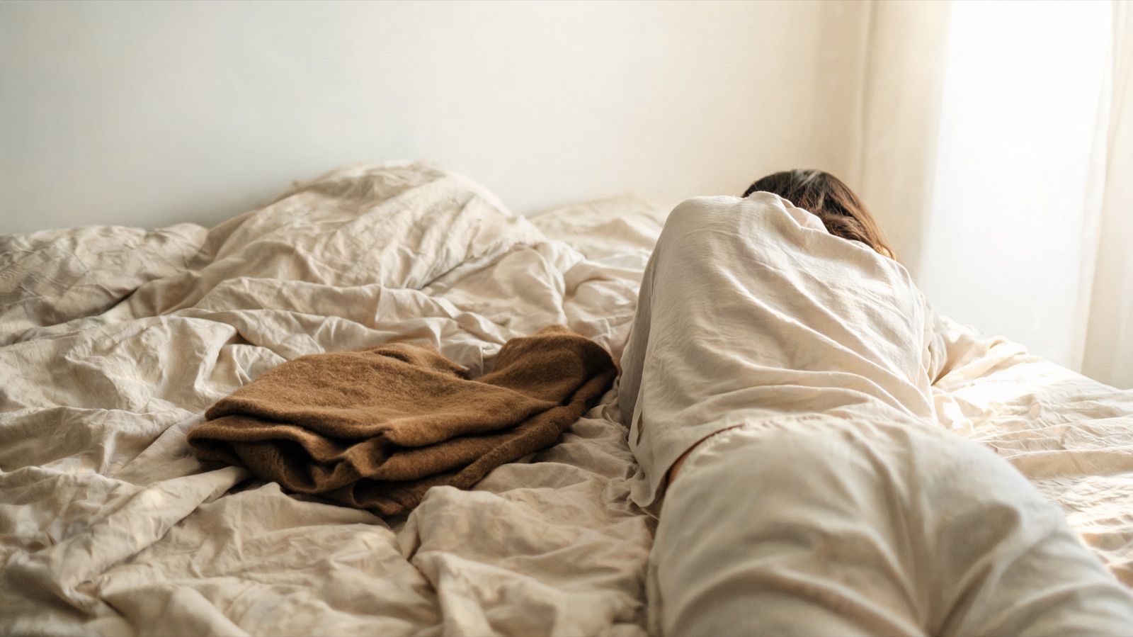 Lenzuola di lino sfatte e una coperta di lana piegata nella luce del primo mattino