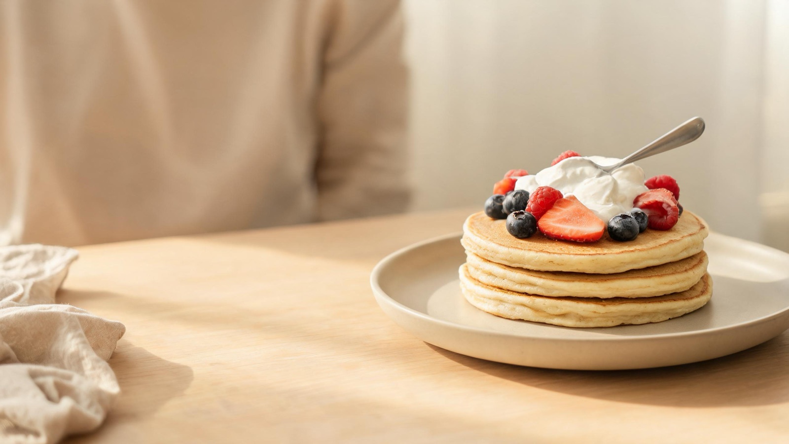 Pila di pancake soffici su un piatto di ceramica con frutti di bosco e yogurt