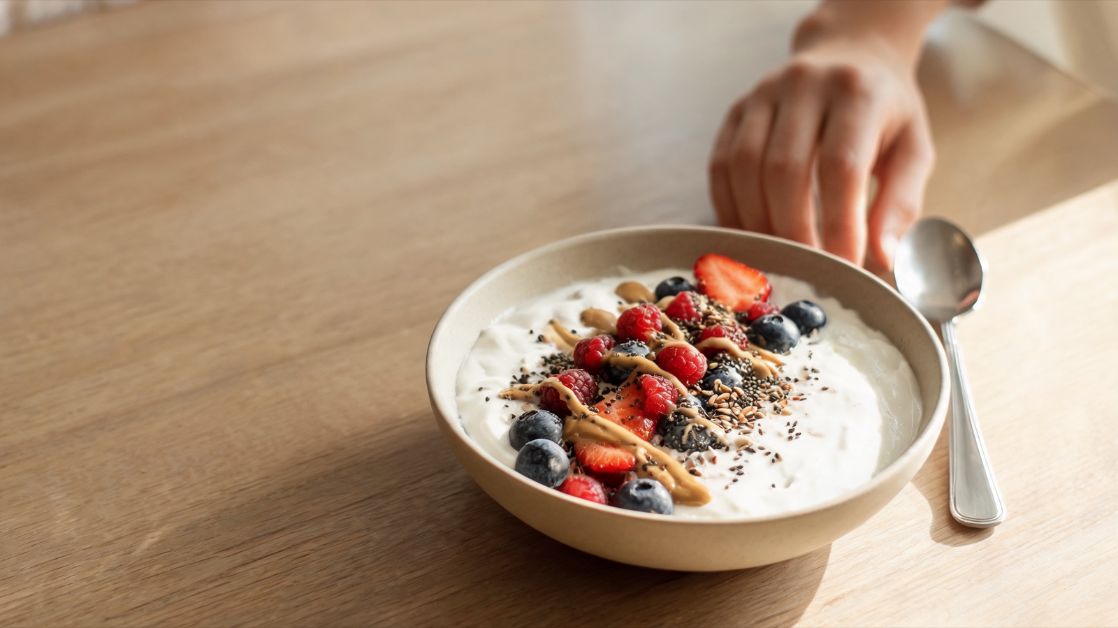 Ciotola di yogurt con frutti di bosco, semi e crema di frutta secca su un tavolo di legno