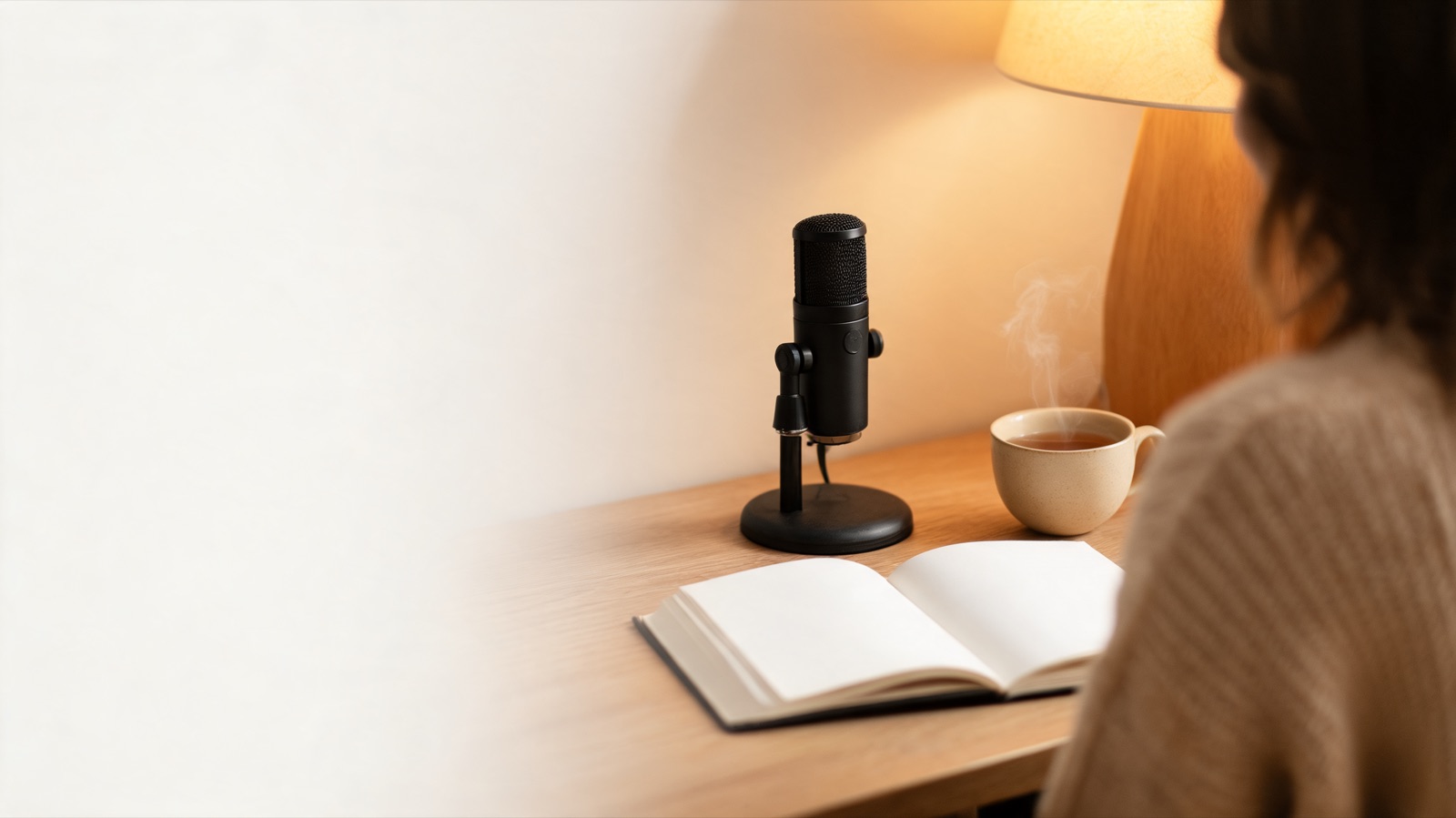 Microfono da studio su una scrivania di legno accanto a un quaderno aperto e una tazza di tè